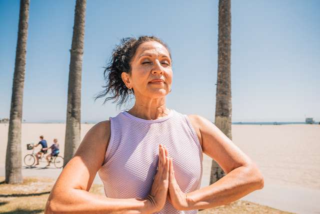 Woman practicing yoga with hands in prayer at sunny beach
