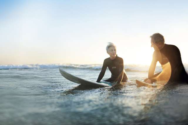 woman and man sitting on surf boards wearing wet suits in the middle of the ocean