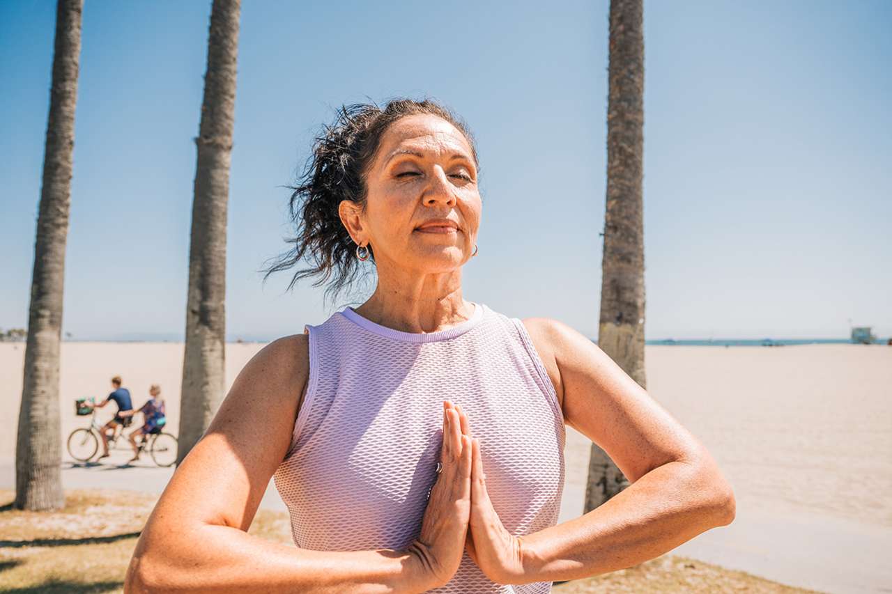 Woman practicing yoga with hands in prayer at sunny beach
