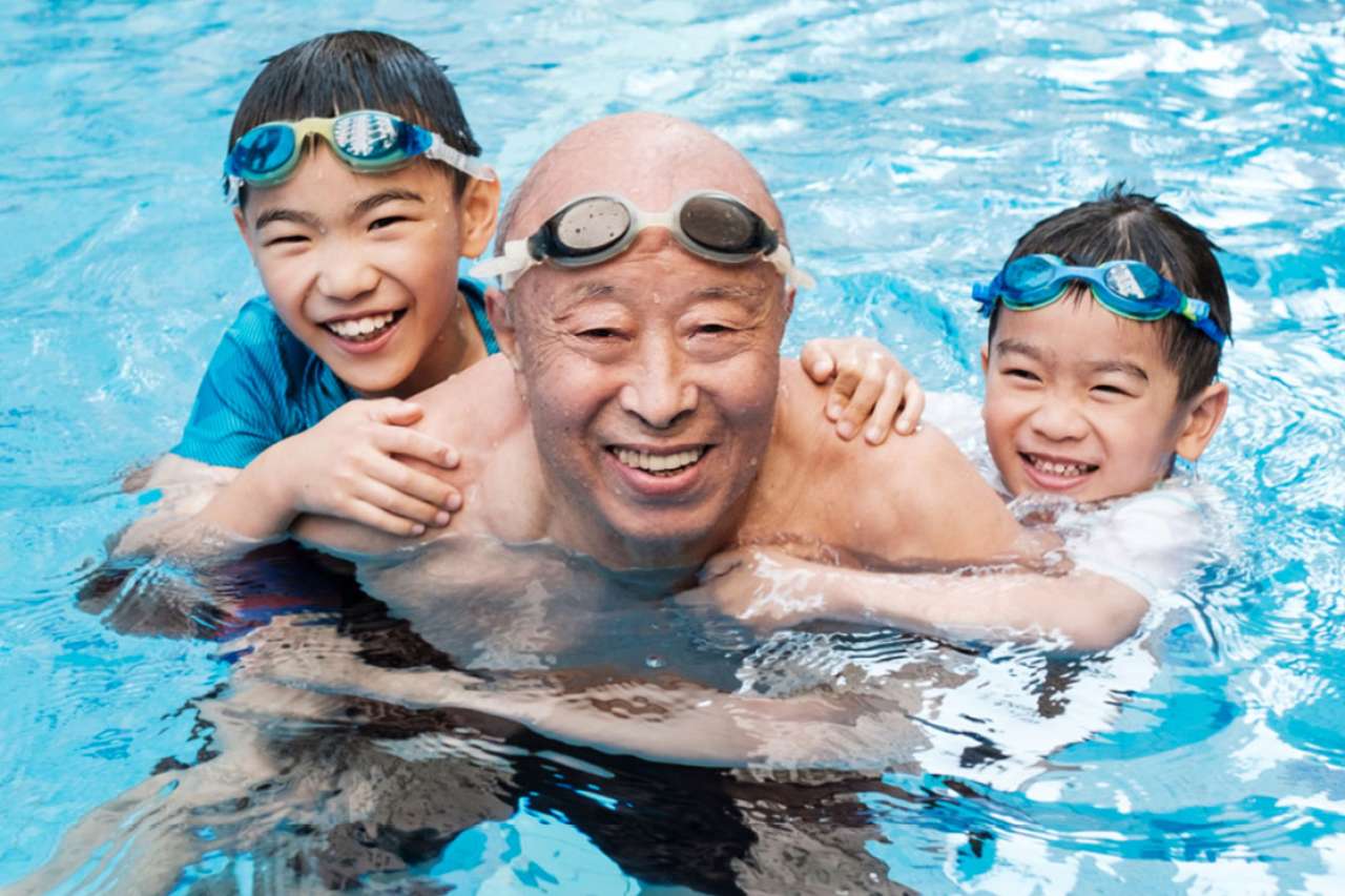 Older male swimming with grandchildren.