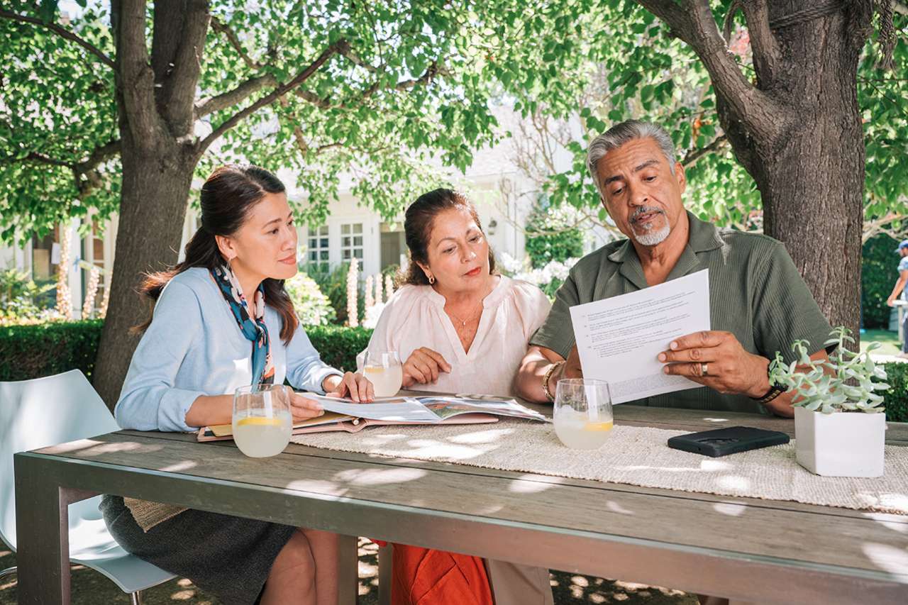 Three people at an outdoor table reviewing documents
